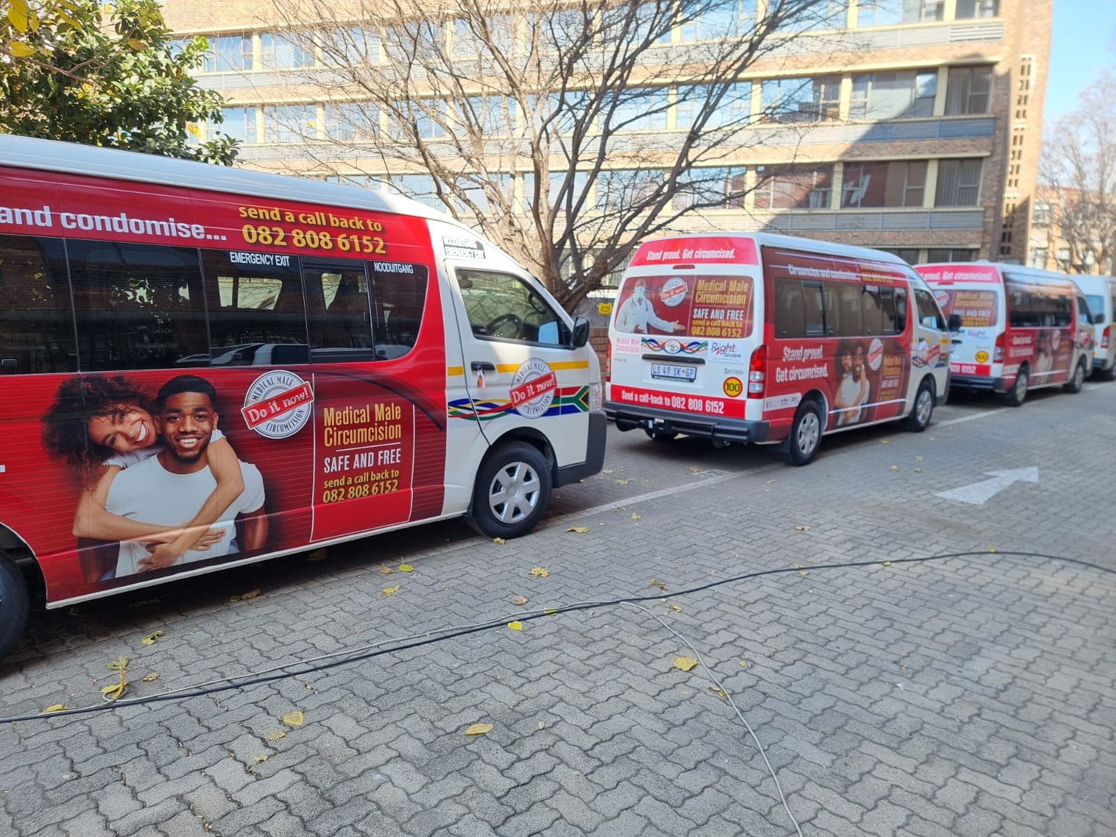 Fleet of minibus taxis in red campaign wraps lined up outside an office block