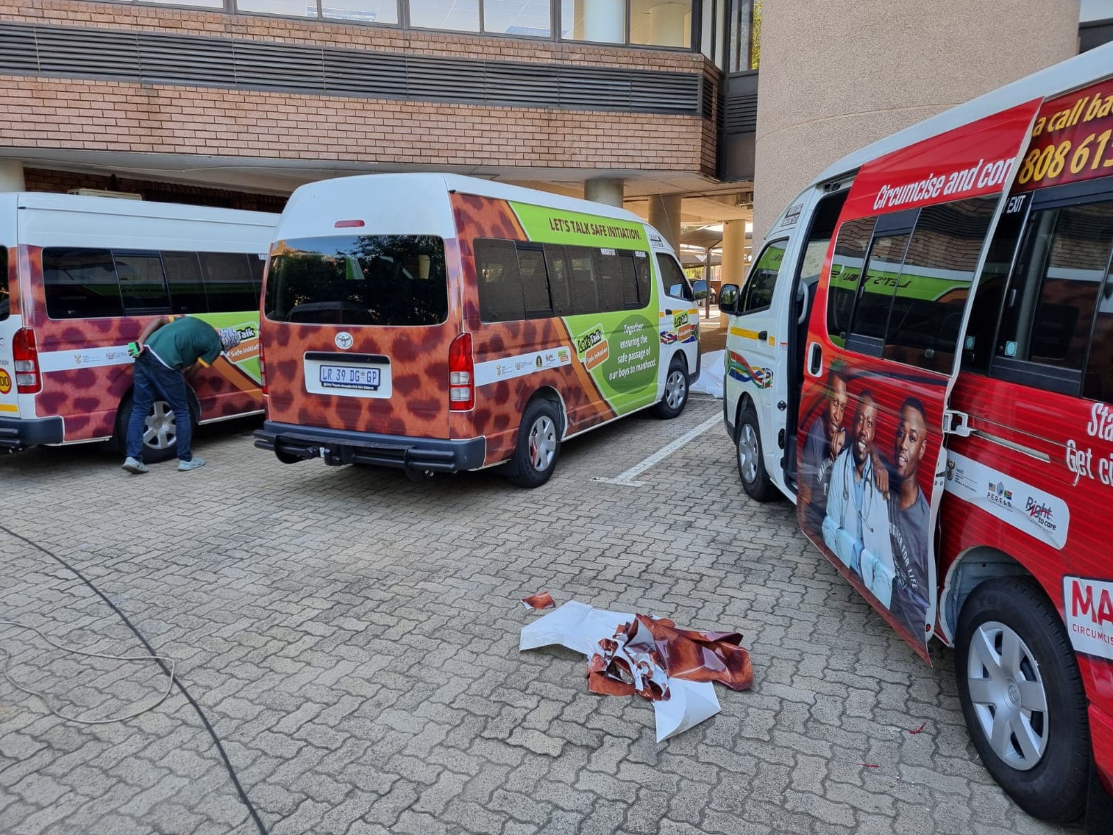 Sportline Digital installer fitting a leopard-print vinyl wrap to a minibus taxi in a parking lot